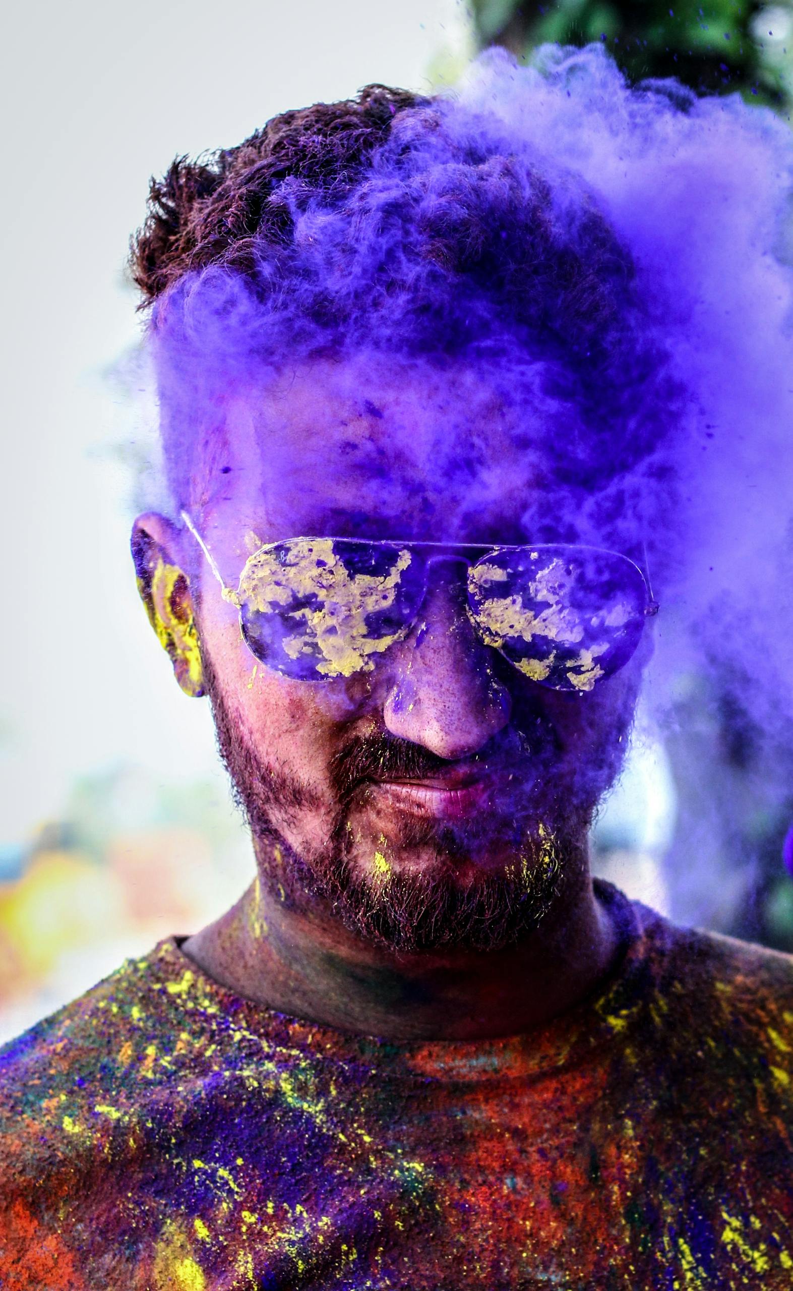 Understanding masculine Themes Vibrant portrait of a man celebrating Holi with colorful powder and sunglasses outdoors.