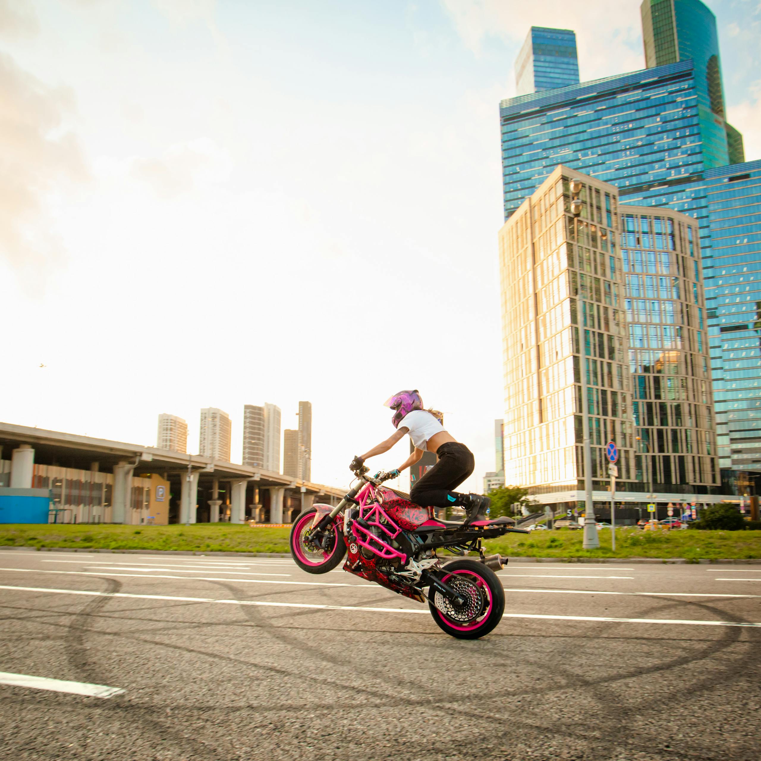 Performance That Feels Like an Upgrade (Because It Is) Woman executes a wheelie on pink motorcycle in front of modern city skyline replicating ScalaHosting Review and its performance.