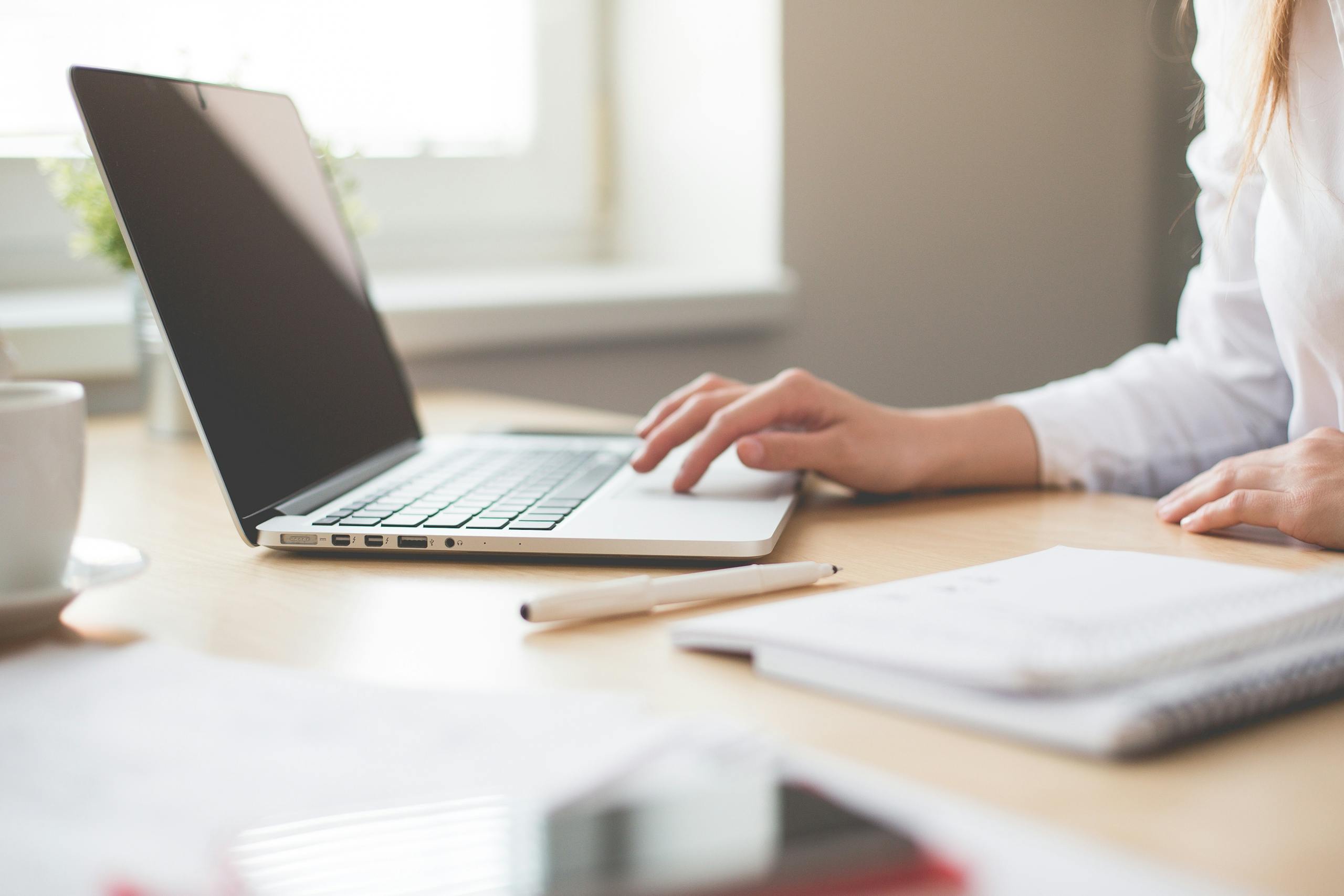 Best WordPress Hosting A businesswoman typing on a laptop at a bright indoor workspace with notebooks and a pen looking for the best wordpress hosting